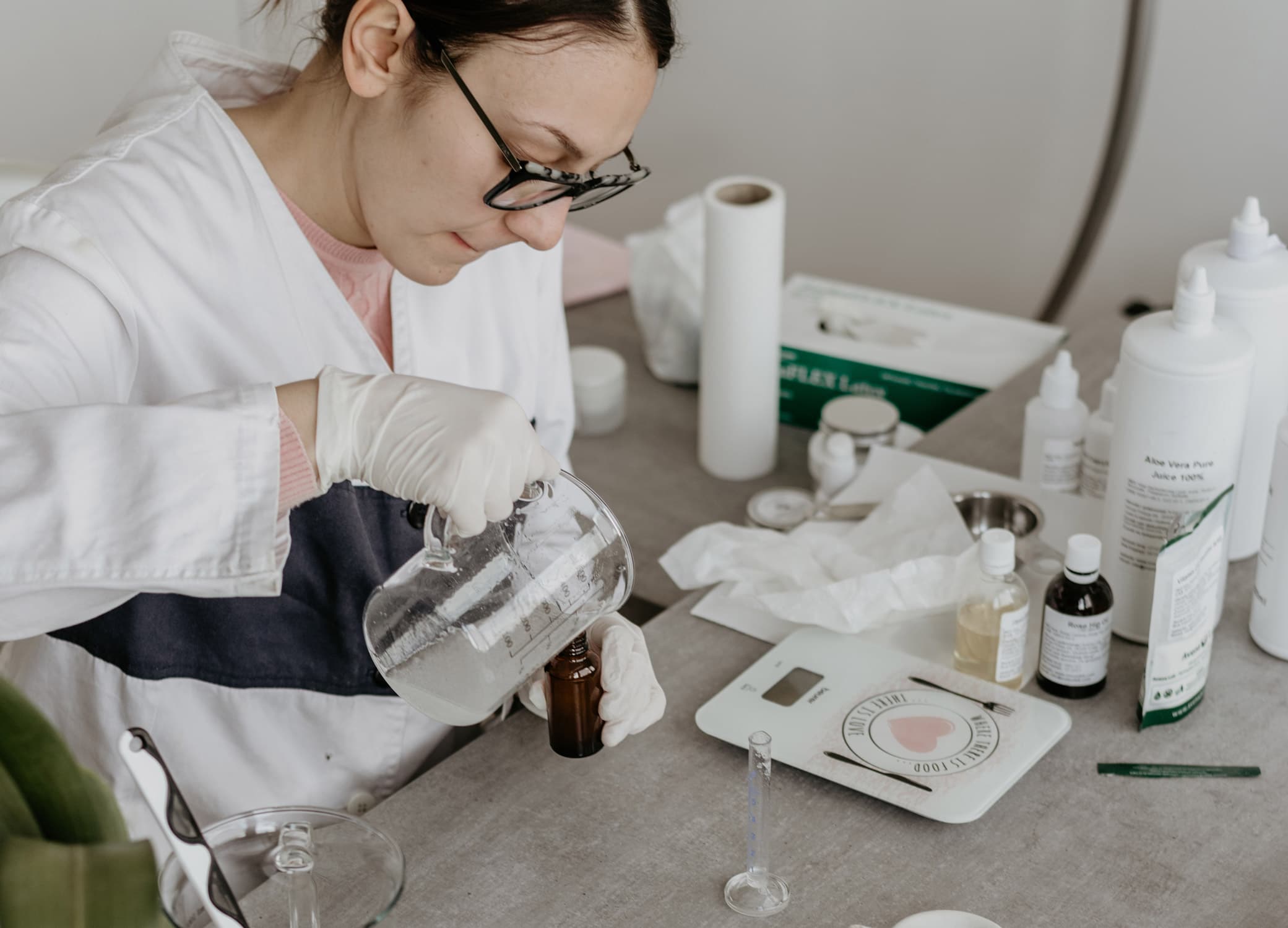 Manufacturer creating a skincare product in a lab with different liquids and mixture tools on table.