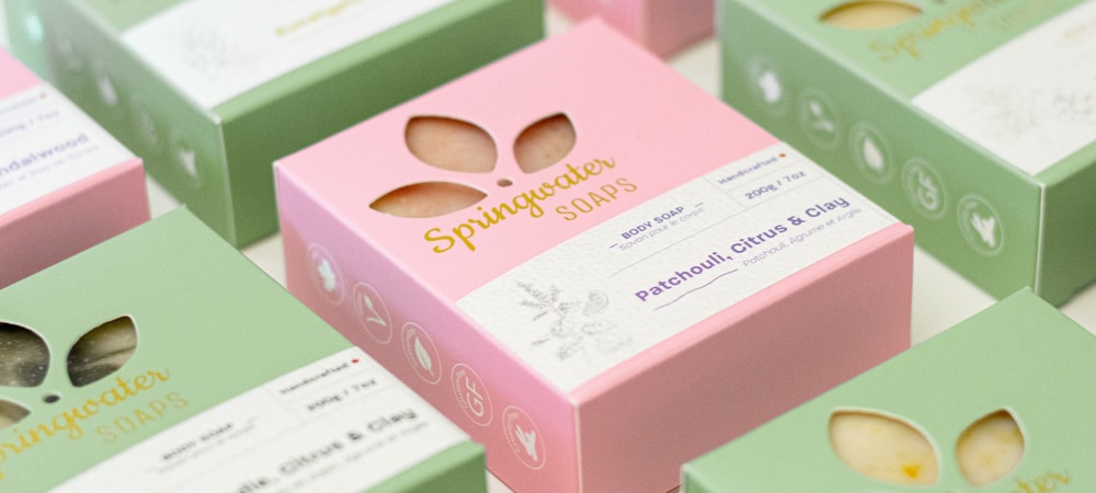 Small business bars of soap lined up in diagonal rows, showcasing up close shots of pastel pink and green retail packaging design boxes.