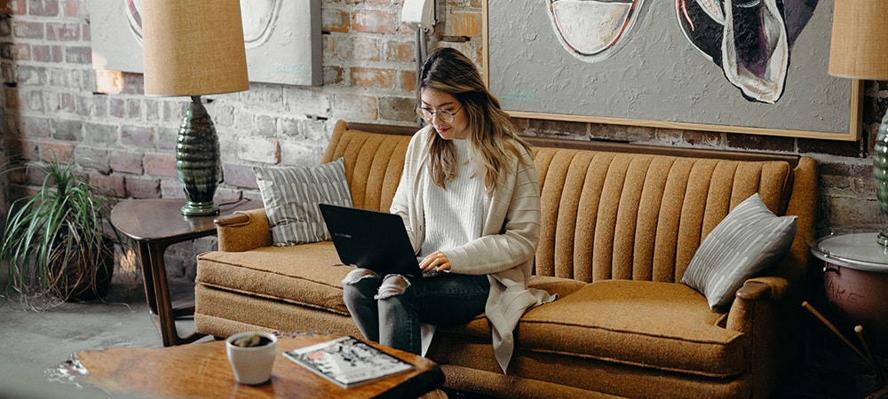 Woman entrepreneur sitting on a couch working on laptop in the comfort of her home.