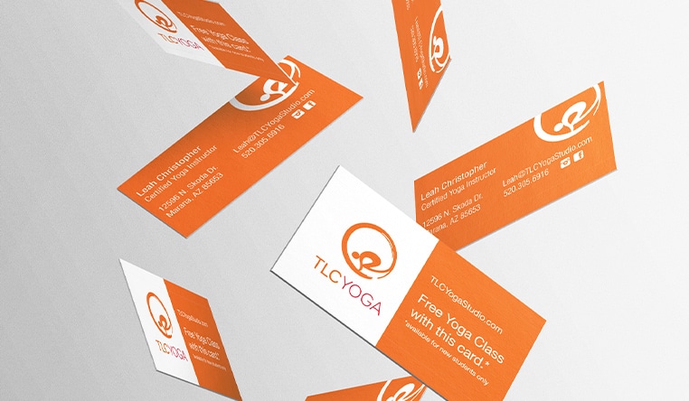 TLC Yoga free-falling business cards in orange and white against a grey background.