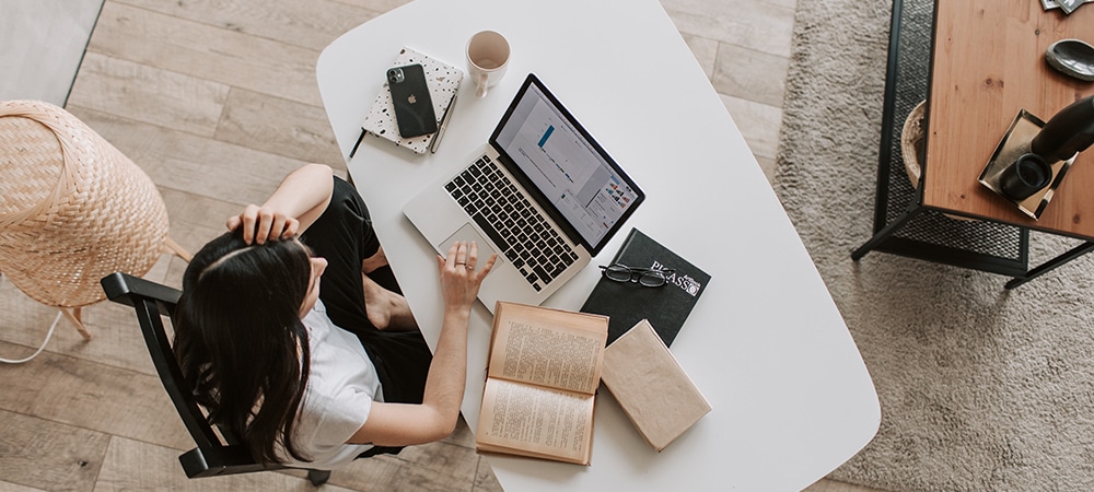 Woman working comfortable at a desk with a laptop, notebooks, iPhone, and other personal accessories. 