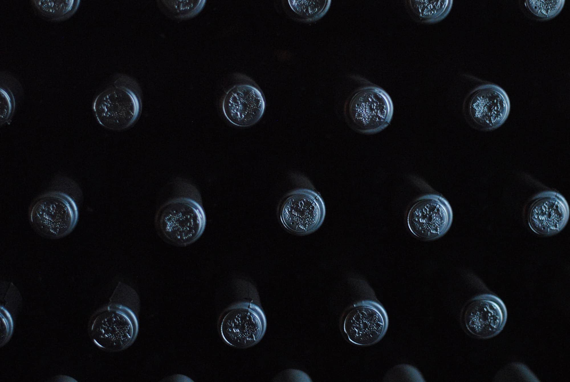 Wine bottles stacked in a distillery with only the tops of the bottles shown.