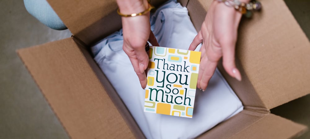 Woman opening up a shipment box with a thank you note and item wrapped inside paper.