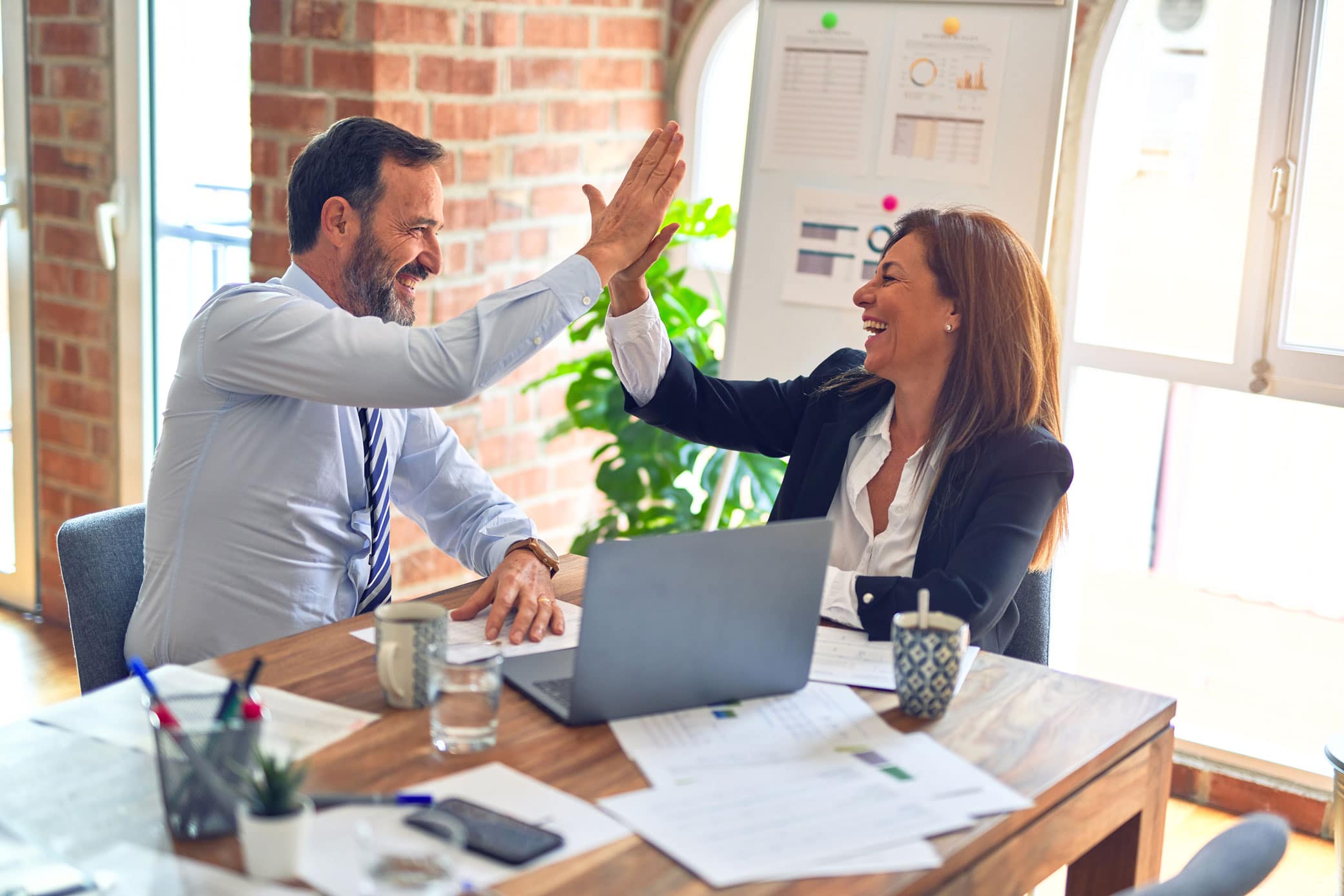 Two entrepreneurs making a deal in an office setting with documents and a laptop on desk.