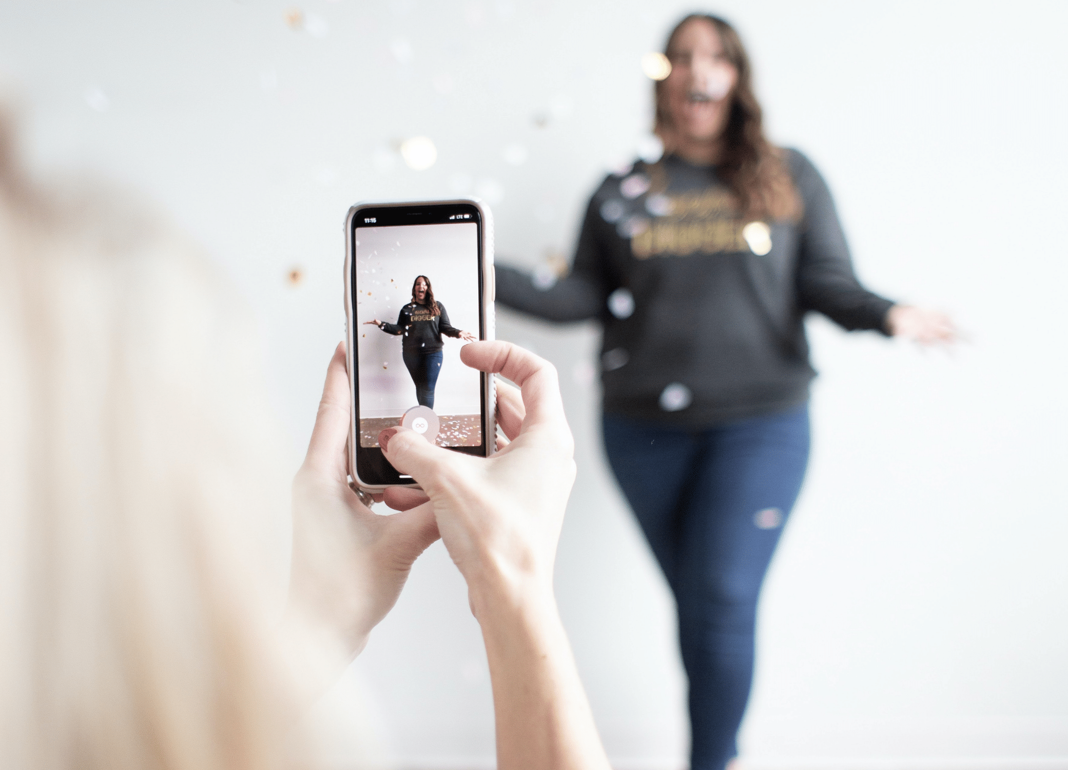 Business woman posing preparing for a TikTok with confetti falling from the ceiling and teammate recording.