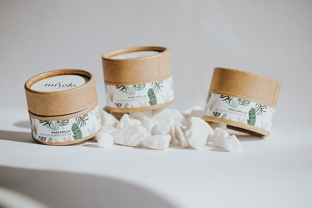 Three products of a cosmetic brand placed on top of some pebbles show the use of paper packaging.