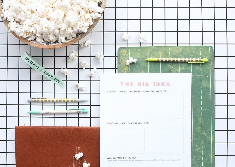 How to Choose a Graphic Designer: A top view of a desk showing a notebook, pens, and a piece of paper asking questions about brand ideas.