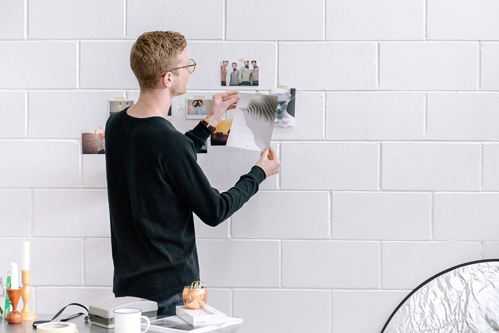 A man pinning pictures to the wall to explore various design services for a brand.