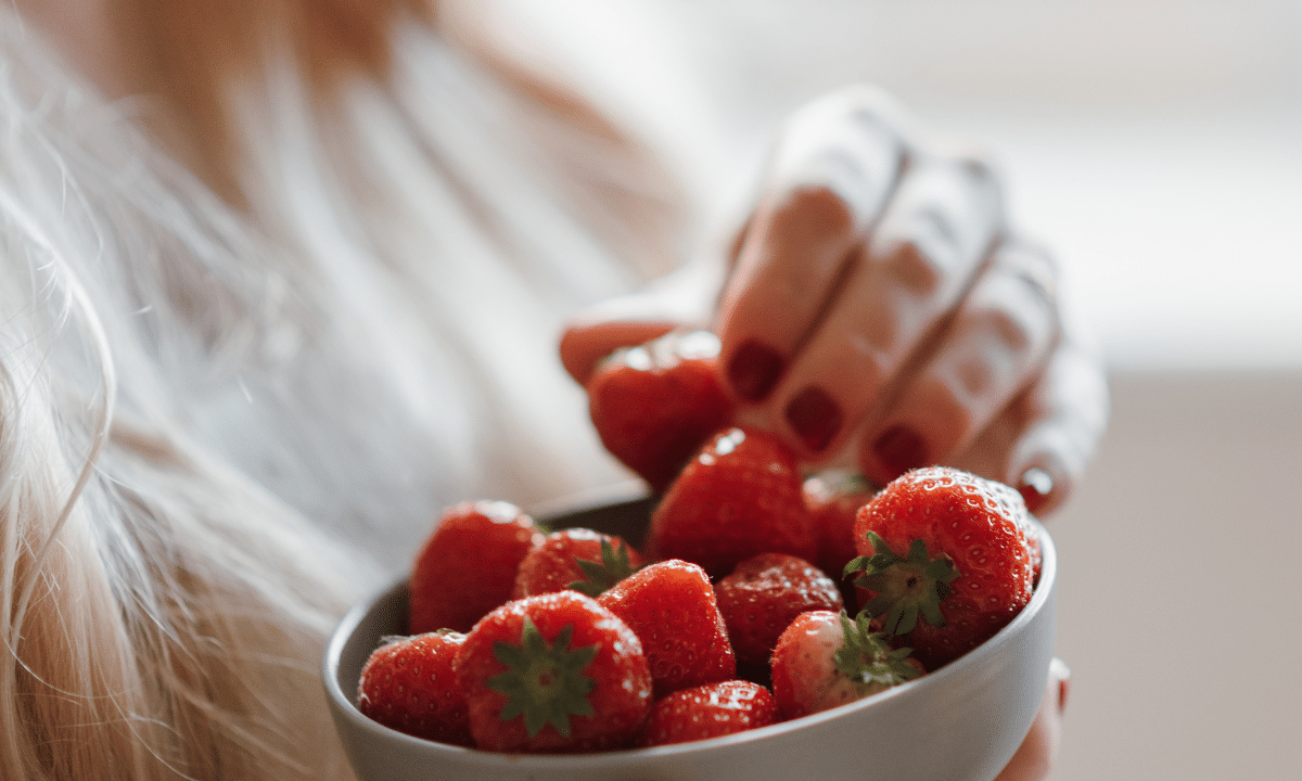 Close up of woman holding a bowl of strawberries and grabbing one.