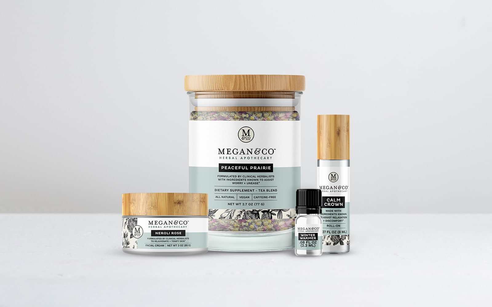 Megan Co the Herbal Apothecary four products in new clear glass packaging with white and dusty blue labels and bamboo lids.