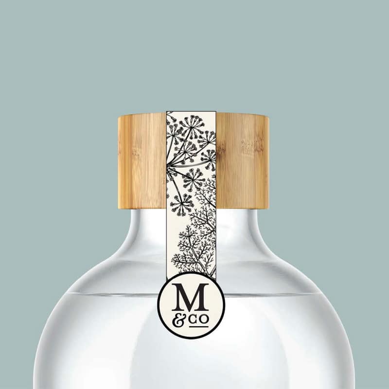 Megan Co the Herbal Apothecary bamboo lid on a glass bottle with a floral illustrated tag with a monogrammed "M & Co".